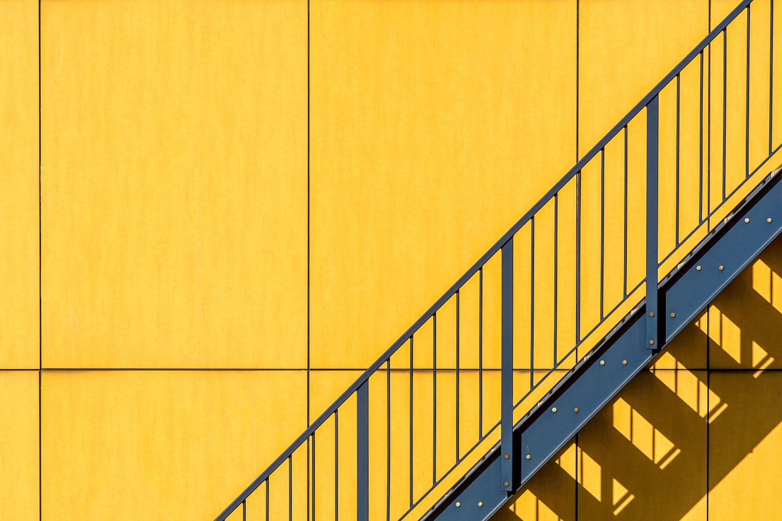 A striking yellow wall with diagonal blue stairs casting shadows, creating geometric patterns.