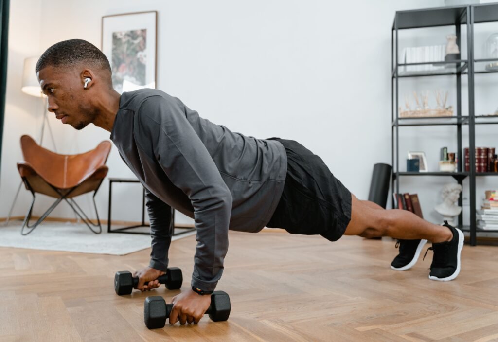 Young man in activewear working out with dumbbells indoors, focused on fitness.